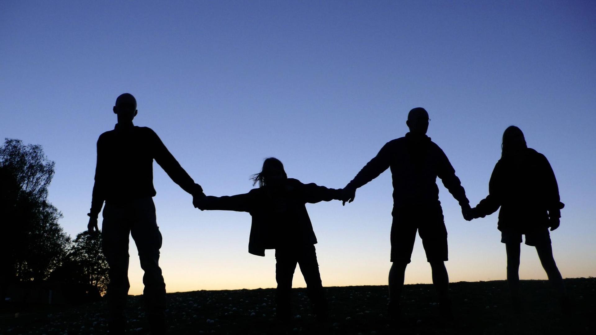 Drei Erwachsene und ein Kind halten sich die Hände, sie sind als Schattenriss vor dem dämmernden Himmel zu sehen. (Symbolbild gesellschaftlicher Zusammenhalt) Drei Erwachsene und ein Kind halten sich die Hände, sie sind als Schattenriss vor dem dämmernden Himmel zu sehen. (Symbolbild gesellschaftlicher Zusammenhalt)