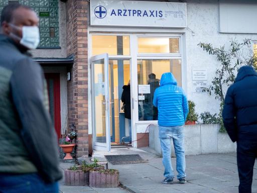 Patienten stehen in großen Abständen zueinander am frühen Morgen vor einer Arztpraxis in Berlin-Lübars an