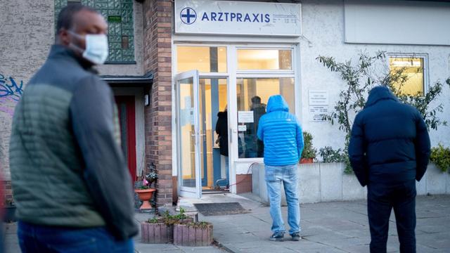 Patienten stehen in großen Abständen zueinander am frühen Morgen vor einer Arztpraxis in Berlin-Lübars an