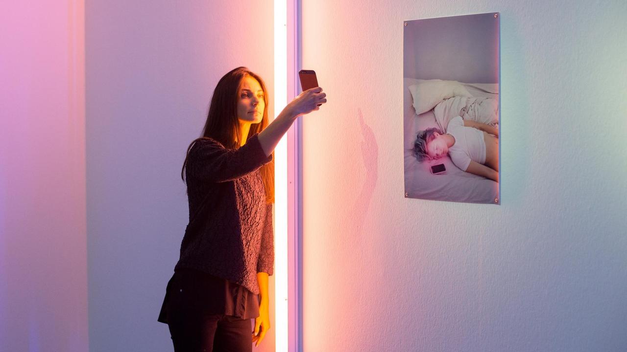 Eine Frau macht in der Ausstellung ein Selfie vor einem Bild an einer Wand Eine Frau macht in der Ausstellung ein Selfie vor einem Bild an einer Wand