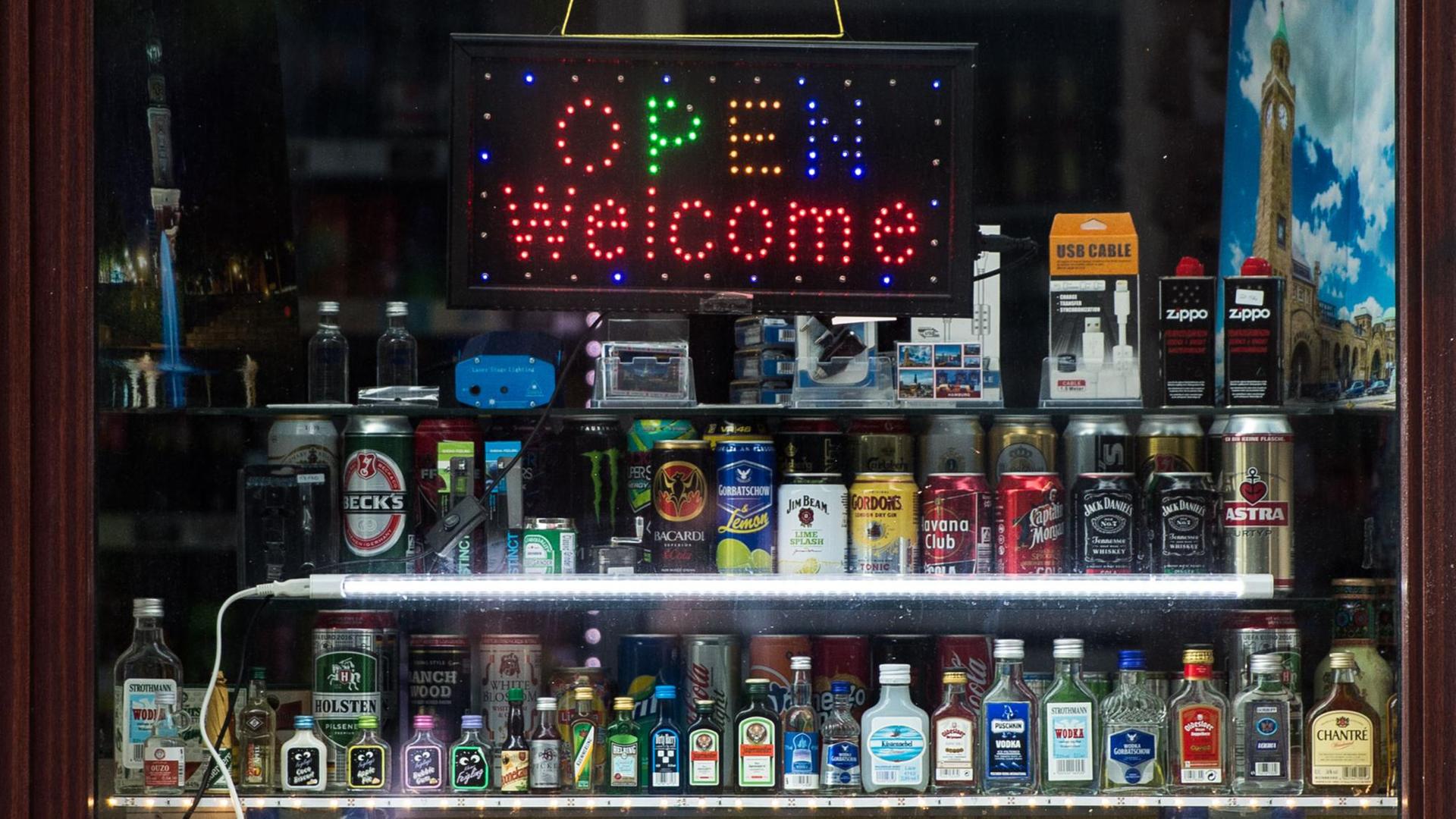 Eine Leuchttafel mit dem Schriftzug "Open Welcome" und zahlreiche alkoholische Getränke stehen am 23.05.2016 in Hamburg in dem Fenster von einem Kiosk.