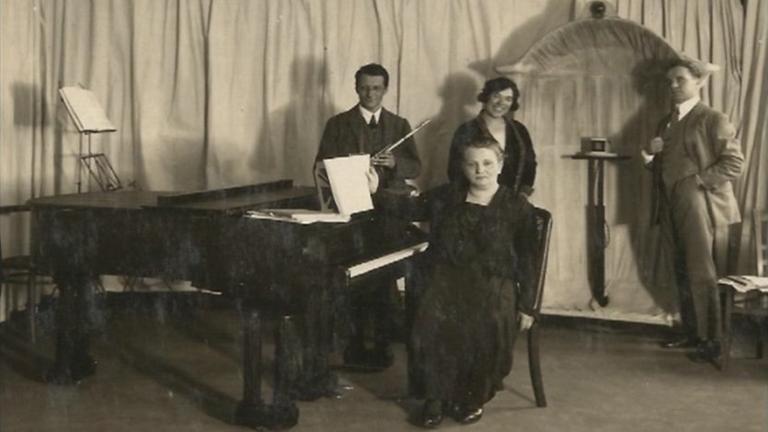 Eine Pianistin in langem Kleid sitzt vor einer weiteren Frau, die von zwei weiteren Musikern umgeben ist in einem Zimmer, das mit Stofflaken ausgekleidet ist, um die Akustik zu verbessern.