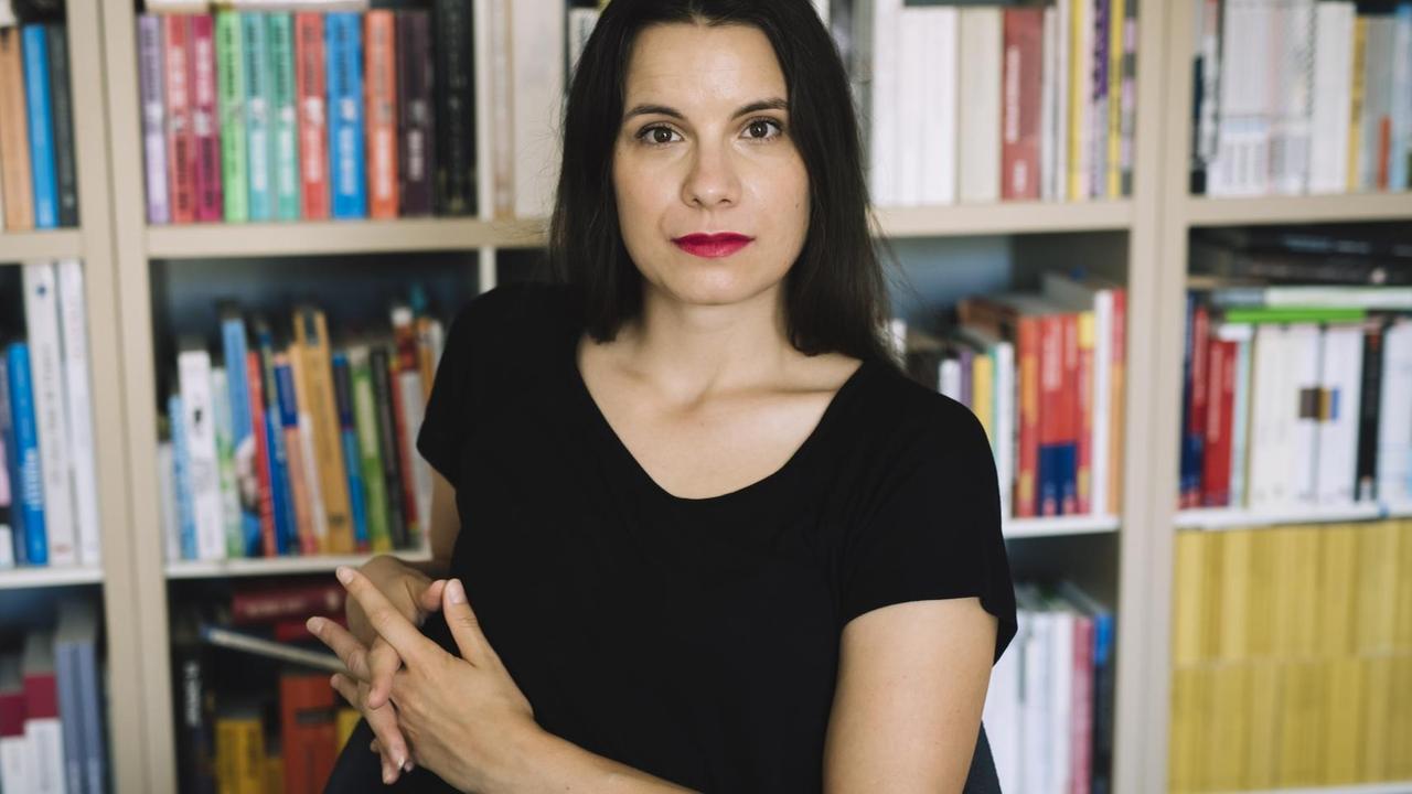 Die Autorin Didi Drobna sitzt vor einem Bücherregal und guckt selbstbewusst in die Kamera Die Autorin Didi Drobna sitzt vor einem Bücherregal und guckt selbstbewusst in die Kamera