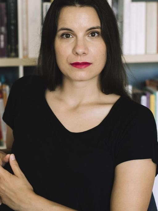 Die Autorin Didi Drobna sitzt vor einem Bücherregal und guckt selbstbewusst in die Kamera
