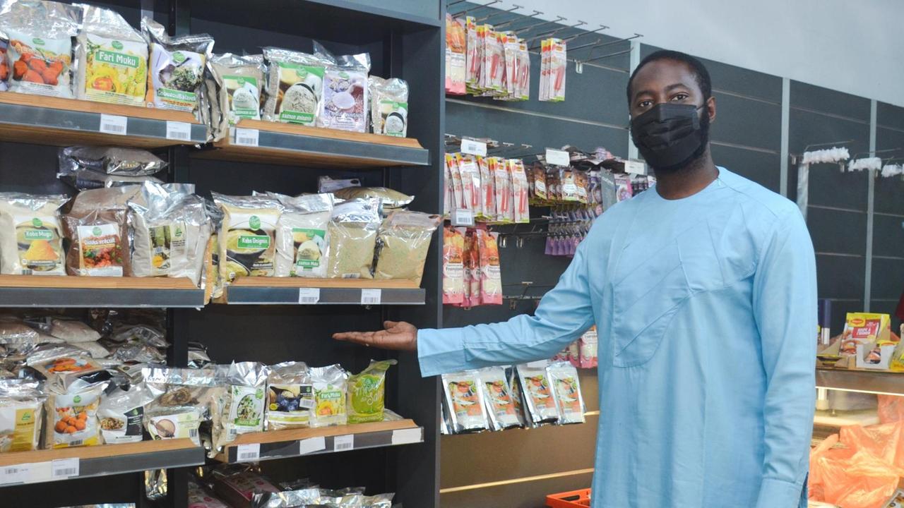 Ein Mann im blauen Hemdkleid und mit Mundschutz, steht vor einem vollen Supermarktregal in Bamako, Mali. Ein Mann im blauen Hemdkleid und mit Mundschutz, steht vor einem vollen Supermarktregal in Bamako, Mali.