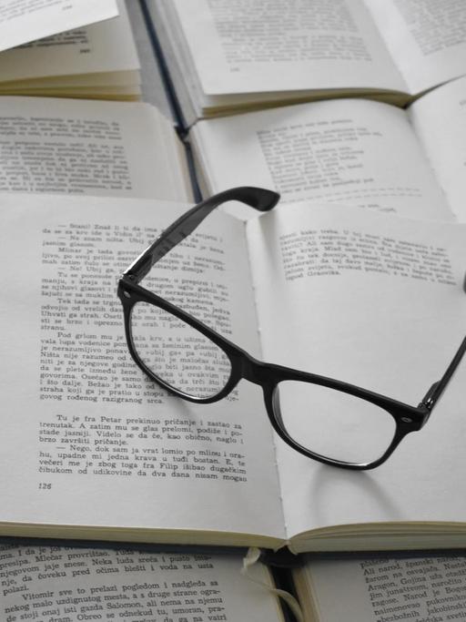 Eine schwarze Brille liegt auf einem Stapel aufgeschlagener Bücher.