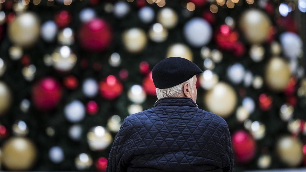 Ein Mann sitzt allein auf einer Bank vor einem geschmückten Weihnachtsbaum. Ein Mann sitzt allein auf einer Bank vor einem geschmückten Weihnachtsbaum.