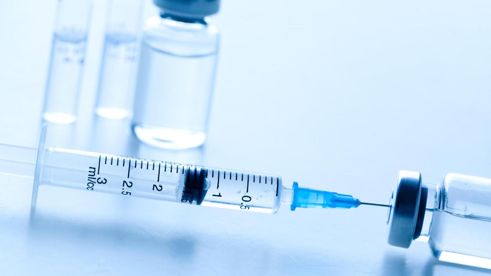 Injektionsnadeln und Ampullen mit Impfstoff liegen auf einem Tisch.
