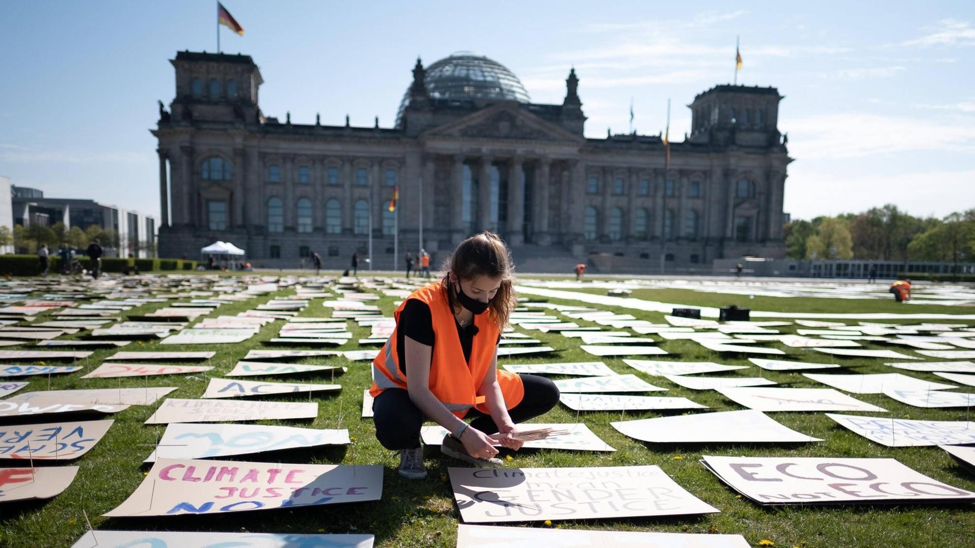 Vor dem Reichstag in Berlin legt eine Frau mit Warnweste und Mundschutz Protestplakate auf die Wiese.
