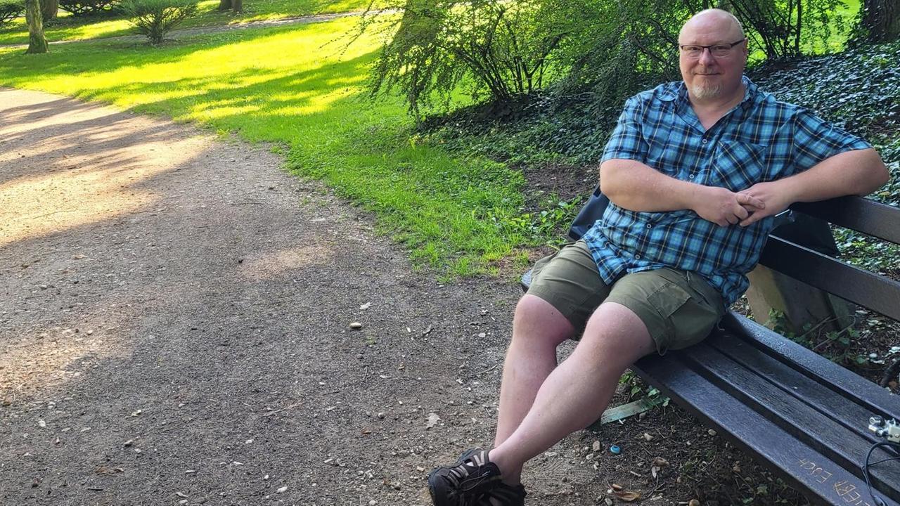 Patrick Bauer sitzt auf einer Parkbank. Patrick Bauer sitzt auf einer Parkbank.