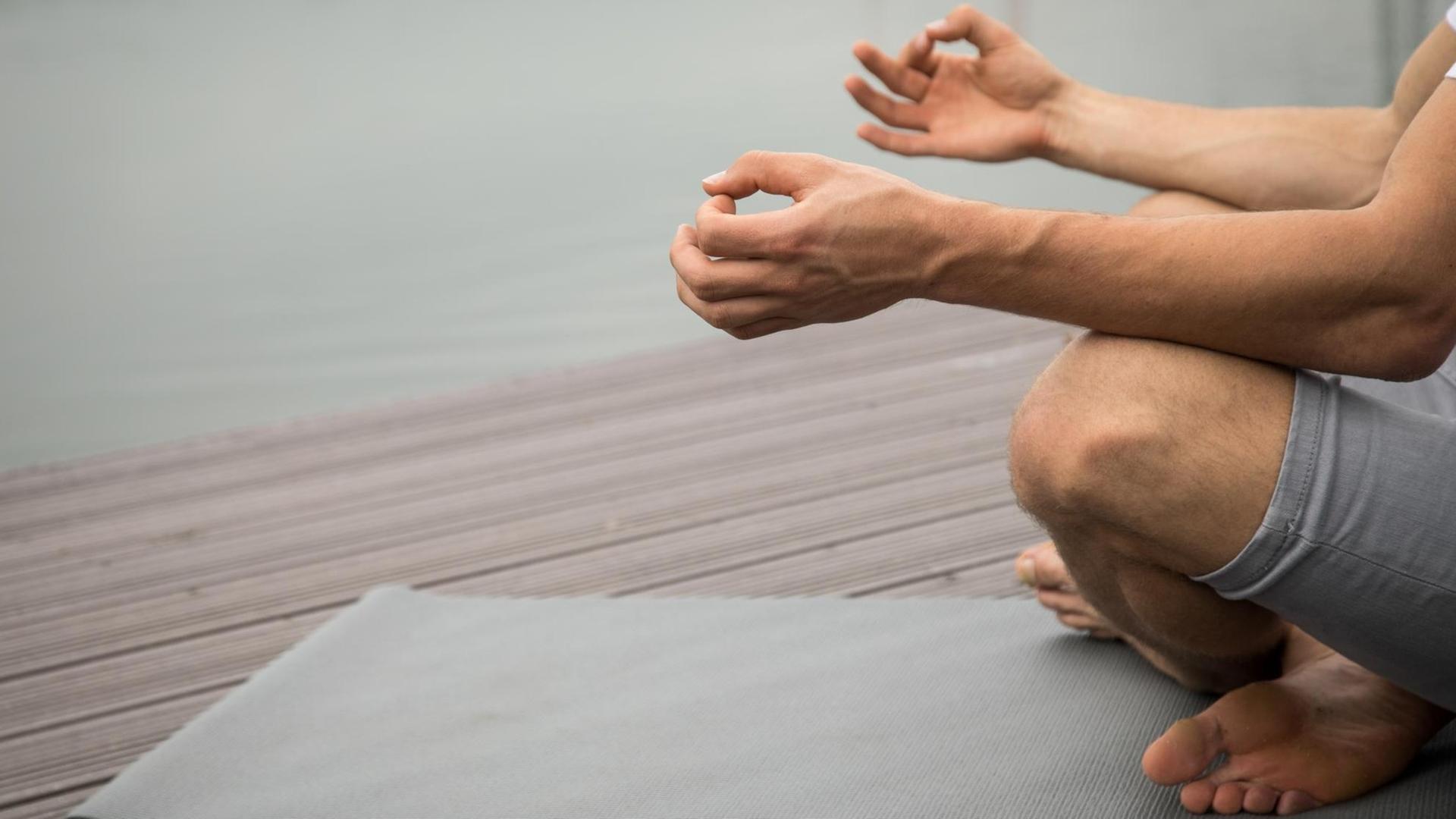 Ein Mann sitzt an einem Seeufer und meditiert auf einer Yogamatte Ein Mann sitzt an einem Seeufer und meditiert auf einer Yogamatte