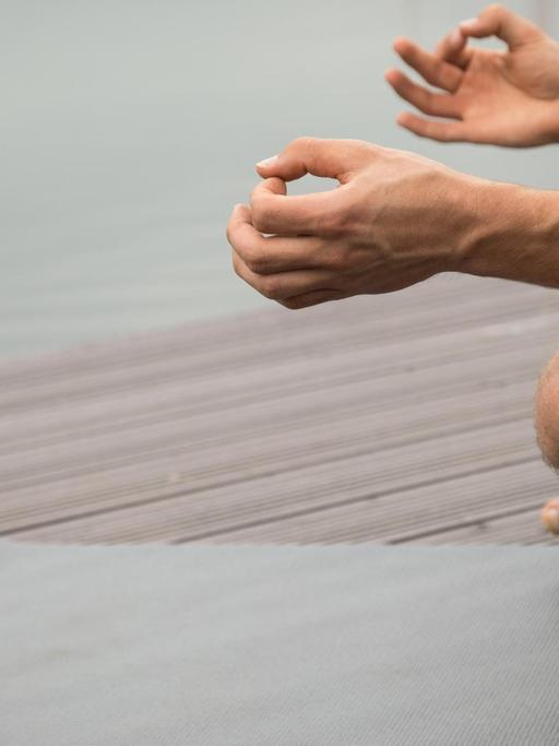 Ein Mann sitzt an einem Seeufer und meditiert auf einer Yogamatte