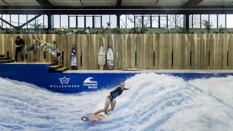 Eine Surferin springt auf einer künstlichen Surfwelle in der Indoor-Surfhalle Wellenwerk.