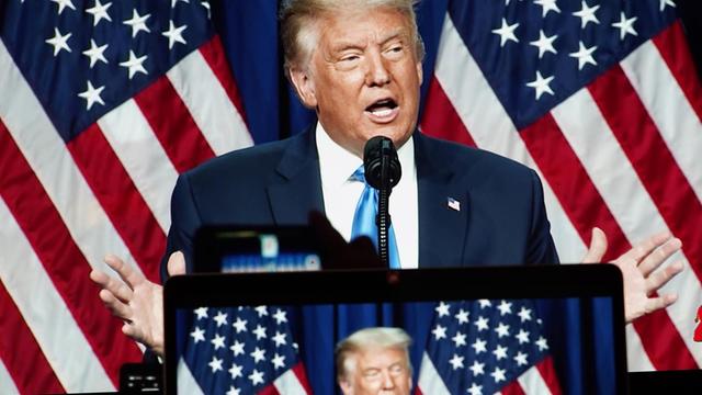 Trump steht am Rednerpult und spricht gestikulierend vor zwei US-Flaggen.