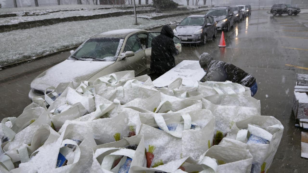 Mitarbeiter der "Food Bank of Lincoln" verteilen während eines Schneesturms Lebensmittel an Personen, die in Autos vorfahren. Mitarbeiter der "Food Bank of Lincoln" verteilen während eines Schneesturms Lebensmittel an Personen, die in Autos vorfahren.