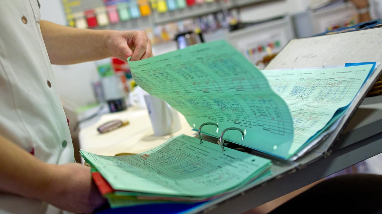 Eine Altenpflegerin in einem Pflegeheim für demenzerkrankte Menschen schaut sich einen Ordner mit Patientenakten an Eine Altenpflegerin in einem Pflegeheim für demenzerkrankte Menschen schaut sich einen Ordner mit Patientenakten an