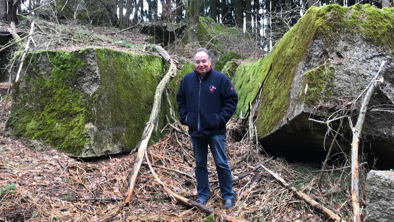 Archivar Dieter Meissle vor Brocken des gesprengten Paraxol Bunkers im Wald, außerhalb des eingezäunten Lerchenberg-Geländes