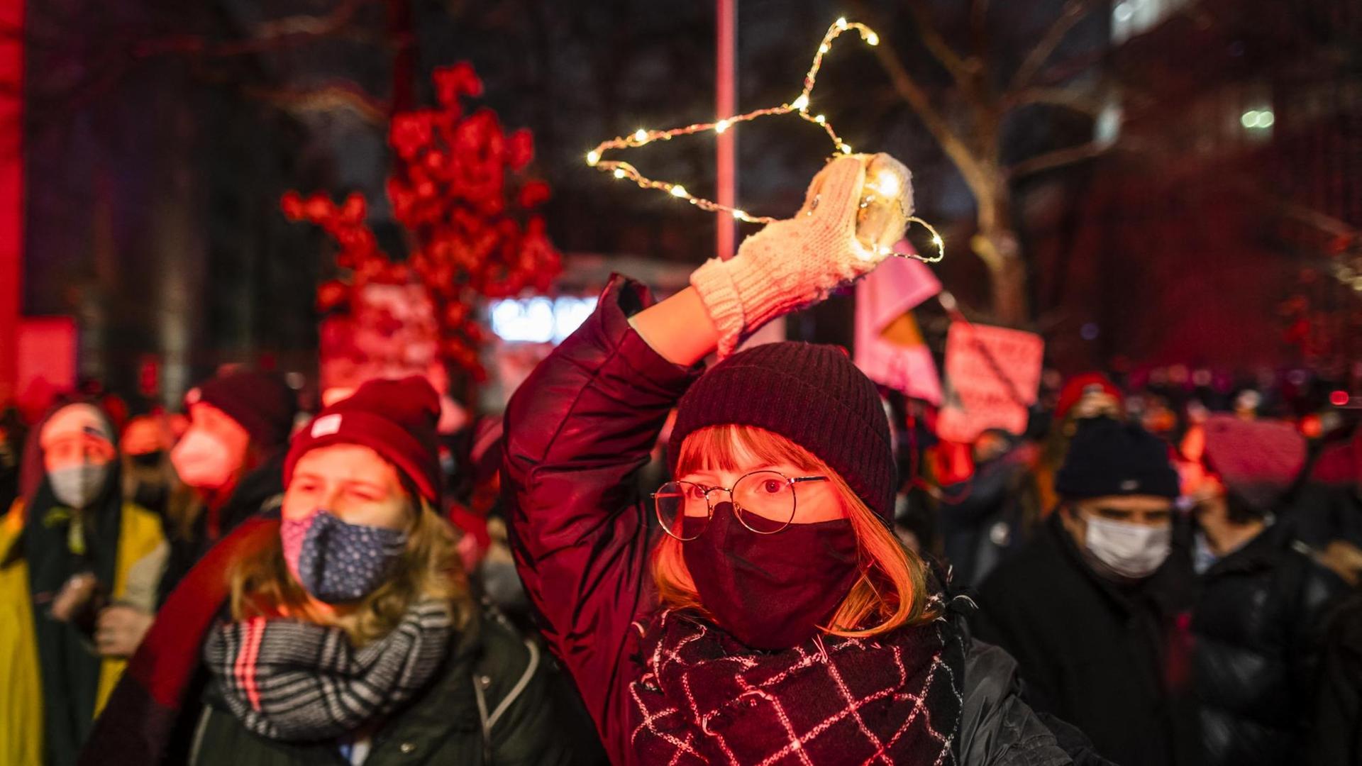 Junge Frauen auf den Strassen von Warschau fordern das Recht auf Abtreibung. Eine Frau hält einen beleuchteten Kleiderbügel in die Luft. Polen, Januar 2021. Junge Frauen auf den Strassen von Warschau fordern das Recht auf Abtreibung. Eine Frau hält einen beleuchteten Kleiderbügel in die Luft. Polen, Januar 2021.