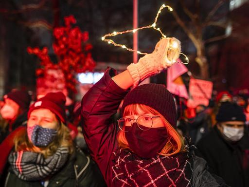 Junge Frauen auf den Strassen von Warschau fordern das Recht auf Abtreibung. Eine Frau hält einen beleuchteten Kleiderbügel in die Luft. Polen, Januar 2021.