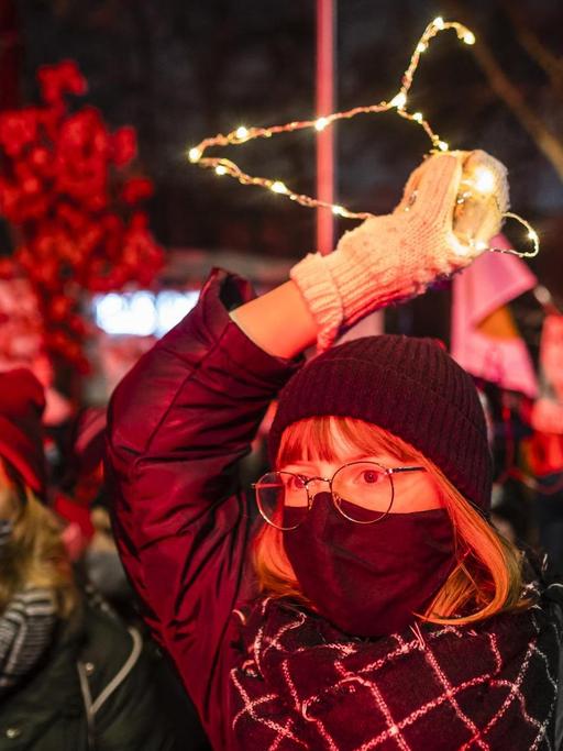 Junge Frauen auf den Strassen von Warschau fordern das Recht auf Abtreibung. Eine Frau hält einen beleuchteten Kleiderbügel in die Luft. Polen, Januar 2021.