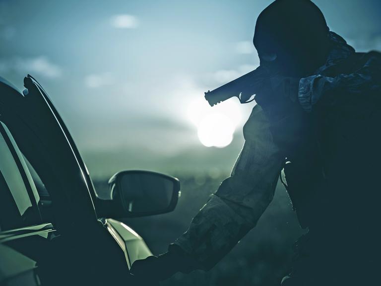 Eine Person mit Maske und Revolver öffnet in der Dunkelheit eine Autotür
