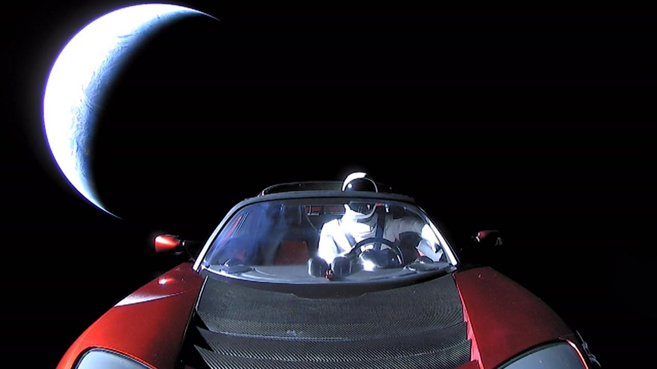 Zusehen ist im Hintergrund der Mond und im Vordergrund eine Auto mit einem Astronauten am Steuer