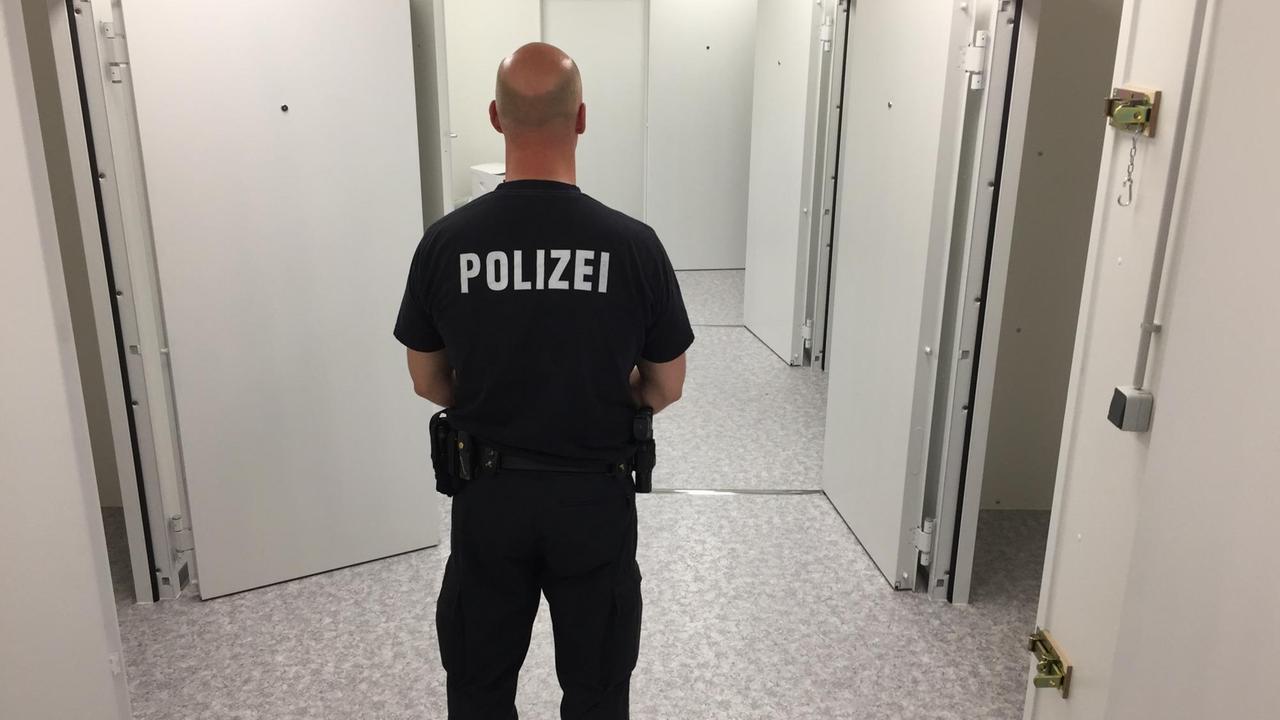 Polizist in Rückansicht vor geöffneten Arrestzellen Polizist in Rückansicht vor geöffneten Arrestzellen