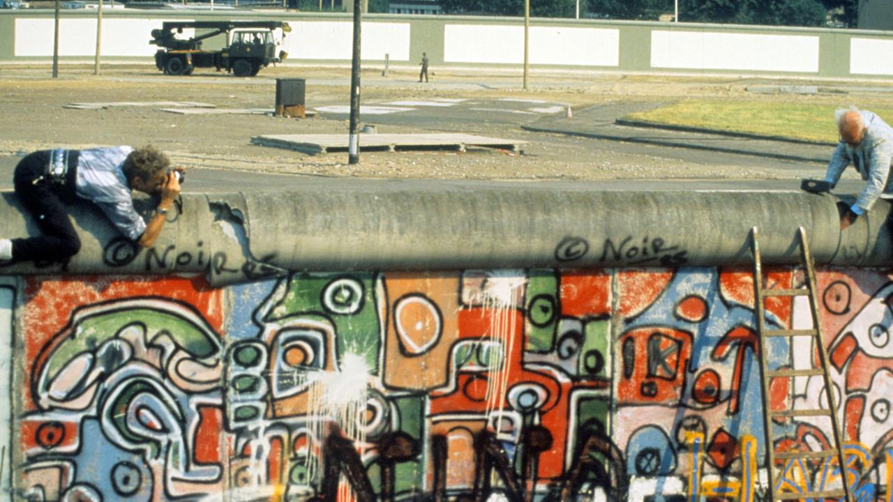 John Runnings demonstriert am 07.08.1986 mit einem Balanceakt gegen den Bau der Berliner Mauer vom 13. August 1961. Mit einem großen Vorschlaghammer führt der 69-jährige Amerikaner vor, was seiner Meinung nach mit dem Bauwerk zu tun sei. John Runnings demonstriert am 07.08.1986 mit einem Balanceakt gegen den Bau der Berliner Mauer vom 13. August 1961. Mit einem großen Vorschlaghammer führt der 69-jährige Amerikaner vor, was seiner Meinung nach mit dem Bauwerk zu tun sei.