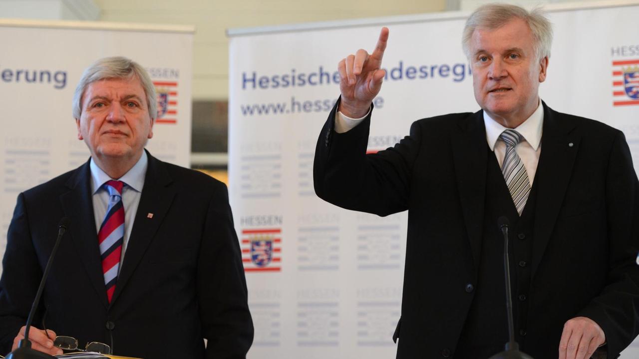 Volker Bouffier und Horst Seehofer stehen nebeneinander vor Aufstellern der Hessischen Landesregierung, Seehofer (rechts) hebt die Hand und spricht.