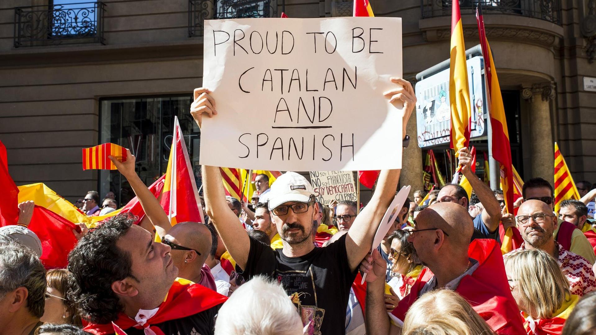 Ein Mann hält in einer Menschenmenge ein Plakat mit der Aufschrift "Stolz, Katalane und Spanier zu sein" in die Höhe. Ein Mann hält in einer Menschenmenge ein Plakat mit der Aufschrift "Stolz, Katalane und Spanier zu sein" in die Höhe.