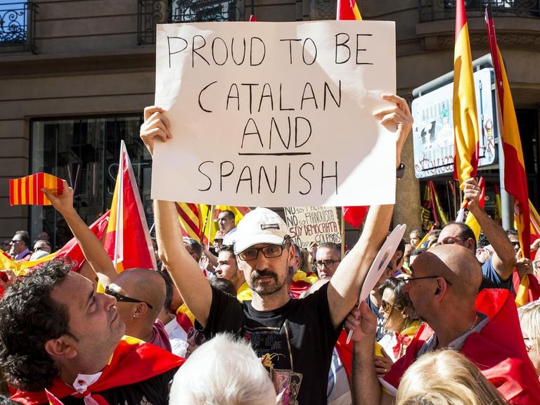 Ein Mann hält in einer Menschenmenge ein Plakat mit der Aufschrift "Stolz, Katalane und Spanier zu sein" in die Höhe.