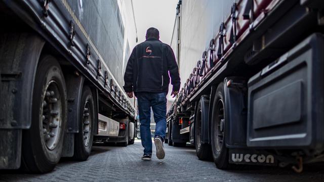 Ein LKW-Fahrer geht zwischen zwei parkenden Lastwagen hindurch.