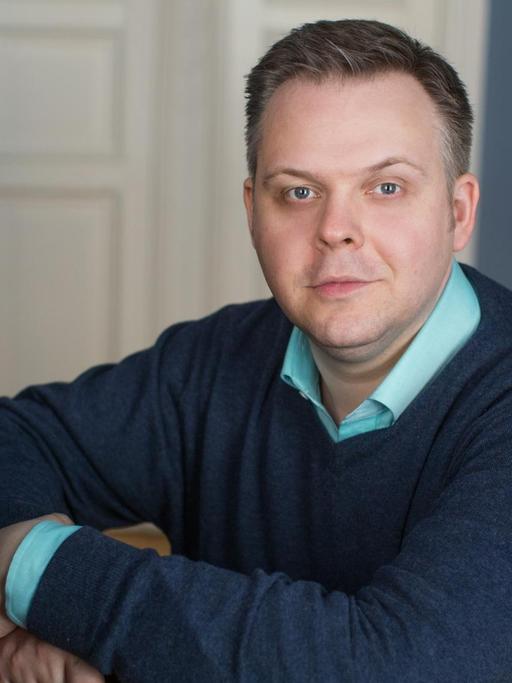 Der Pianist sitzt am heimischen Instrument, das von Bücherregalen umgeben ist.