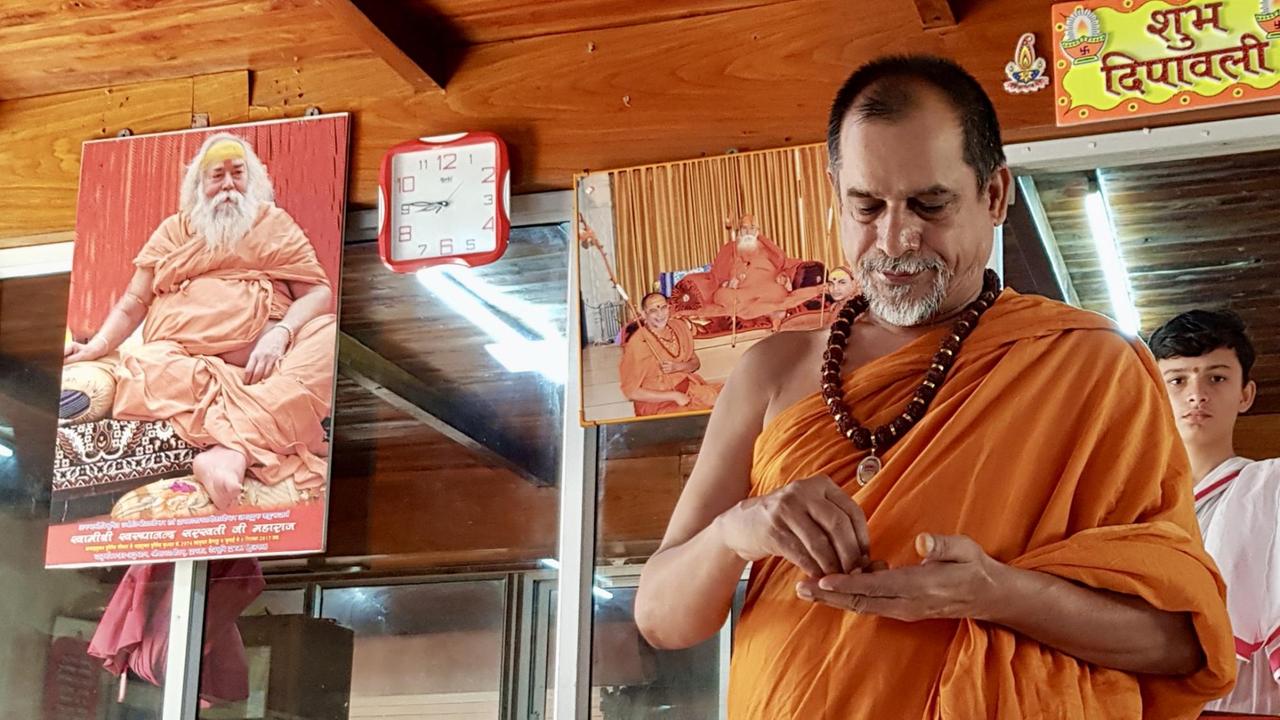 Ein Mann in orangefarbenem Tuch gekleidet steht in einem Raum, der mit Bildnissen von anderen Mönchen geschmückt ist. Ein Mann in orangefarbenem Tuch gekleidet steht in einem Raum, der mit Bildnissen von anderen Mönchen geschmückt ist.