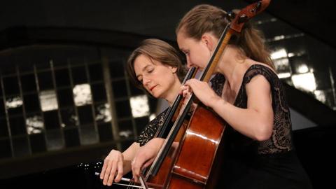 Zwei Cellistinnen in schwarzer Konzertkleidung streichen mit dem Bogen über ihre Instrumente..
