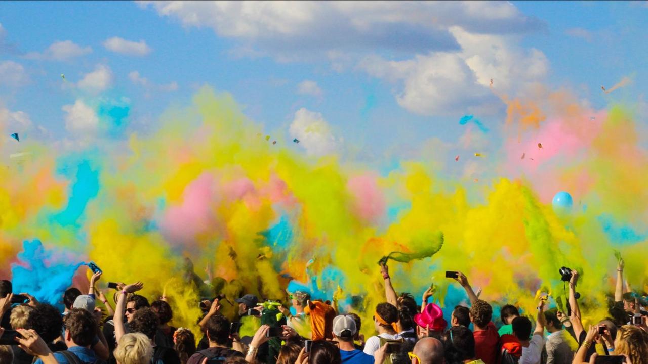 Tanzende Menschen vor blauem Himmel in dem sich buntes Puder verteilt. Tanzende Menschen vor blauem Himmel in dem sich buntes Puder verteilt.