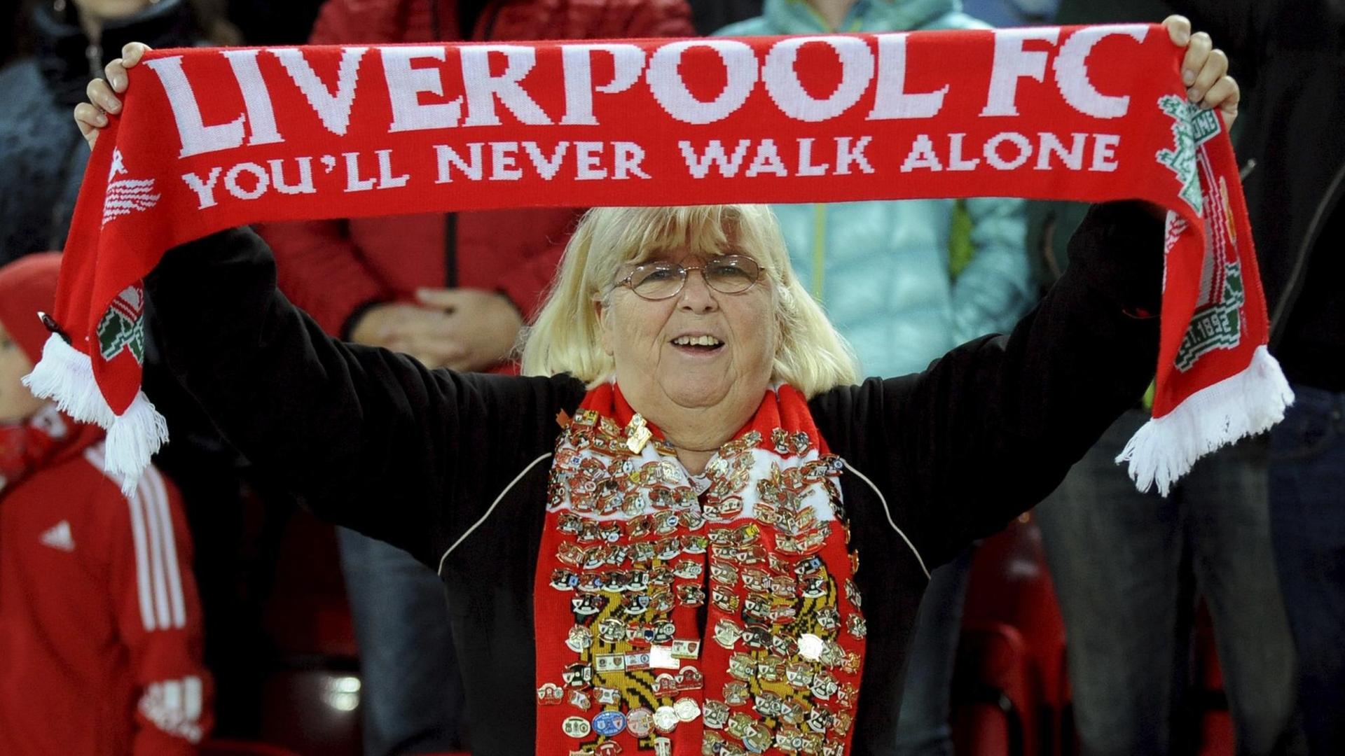 Das Foto zeigt einen weiblichen Fan des FC Liverpool, die ihren Fan-Schal hochhält. Darauf steht: You'll never walk alone.