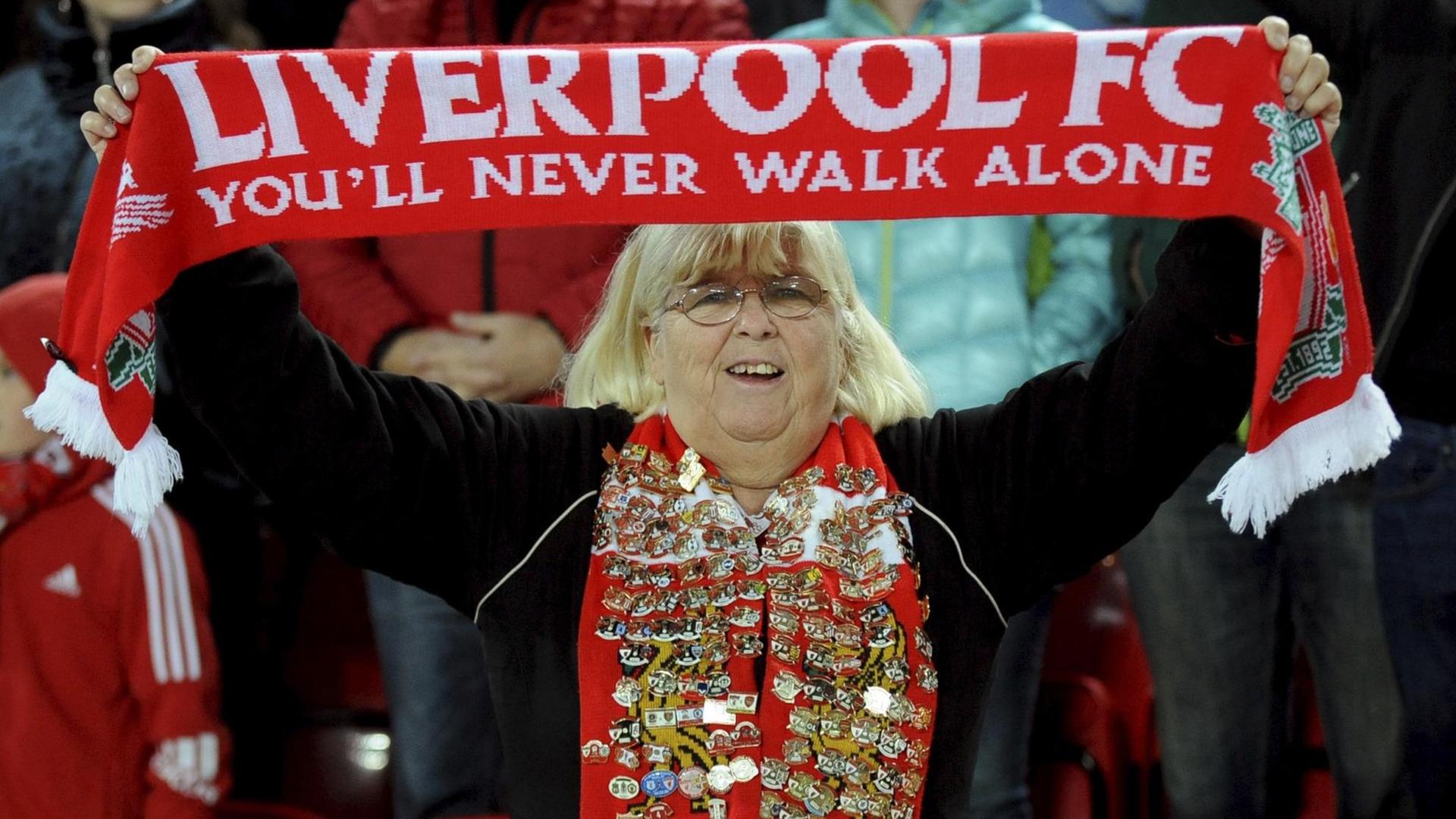 Das Foto zeigt einen weiblichen Fan des FC Liverpool, die ihren Fan-Schal hochhält. Darauf steht: You'll never walk alone. Das Foto zeigt einen weiblichen Fan des FC Liverpool, die ihren Fan-Schal hochhält. Darauf steht: You'll never walk alone.