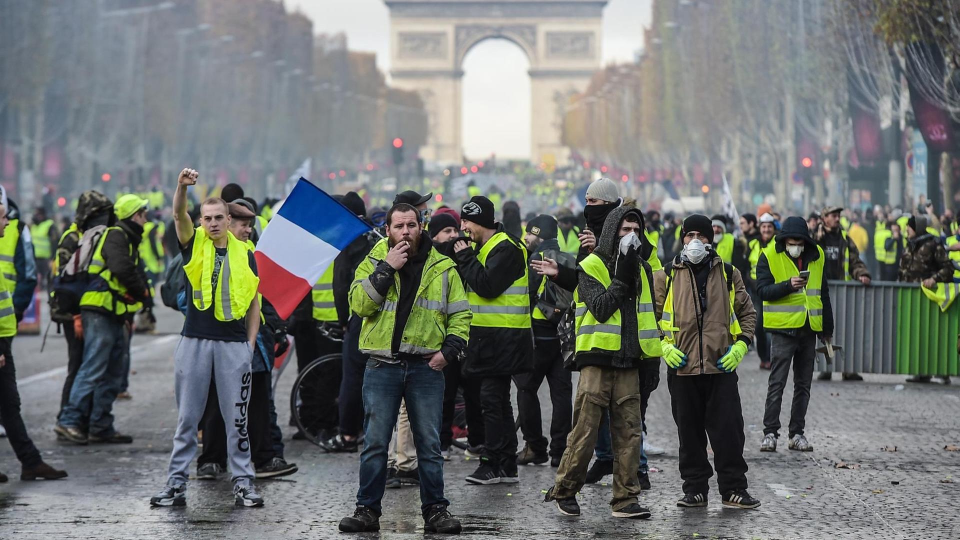Hunderte Demonstranten mit gelben Westen auf der Straße. Im Hintergrund ist der Triumphbogen zu sehen. Hunderte Demonstranten mit gelben Westen auf der Straße. Im Hintergrund ist der Triumphbogen zu sehen.