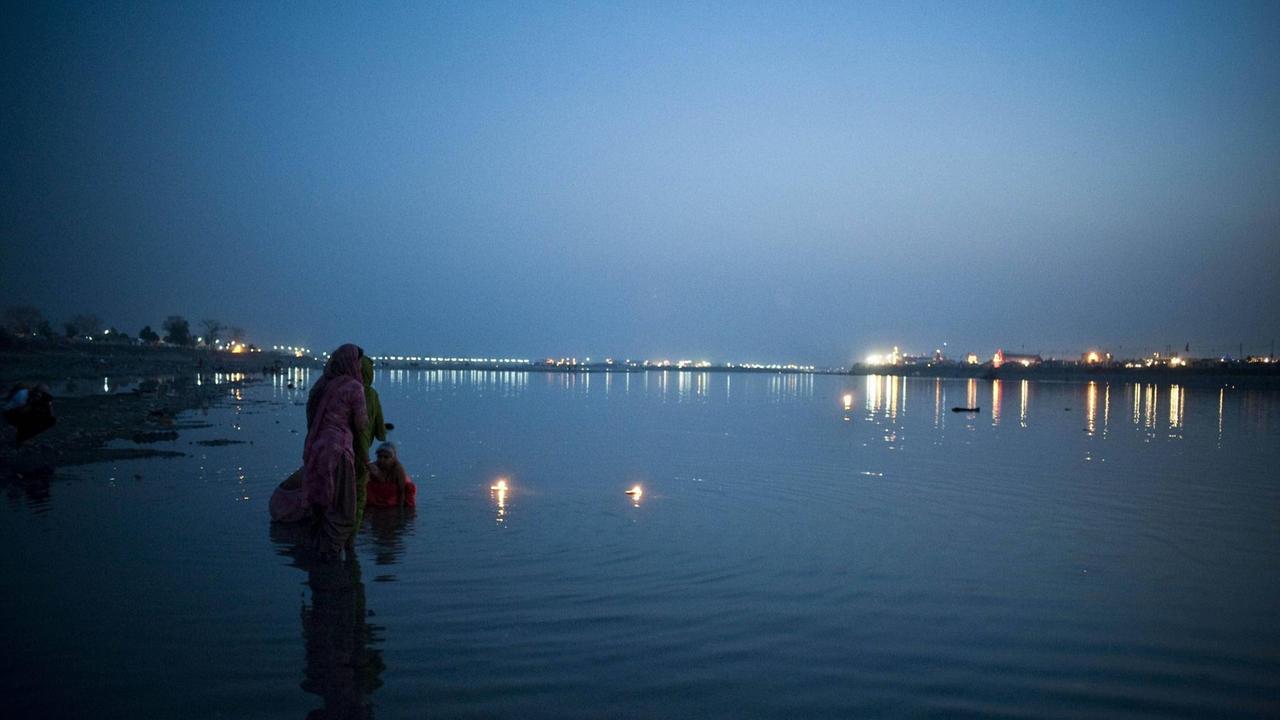 Zwei Frauen und ein Kind baden angezogen am Ufer eines Flußes in der Dämmerung (Indien, Hadriwar). Zwei Frauen und ein Kind baden angezogen am Ufer eines Flußes in der Dämmerung (Indien, Hadriwar).