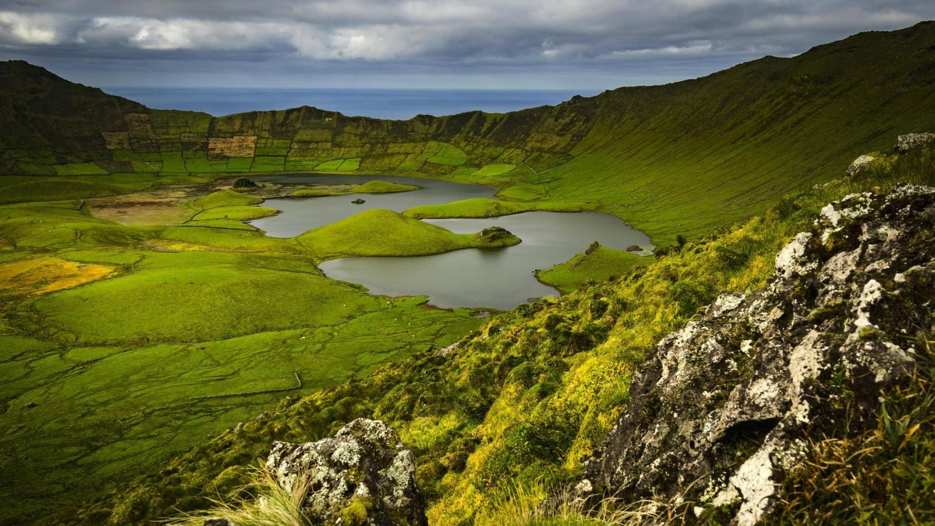 Epischer Panorama über einen grünen Vulkankrater, in dessen Mitte sich ein See befindet