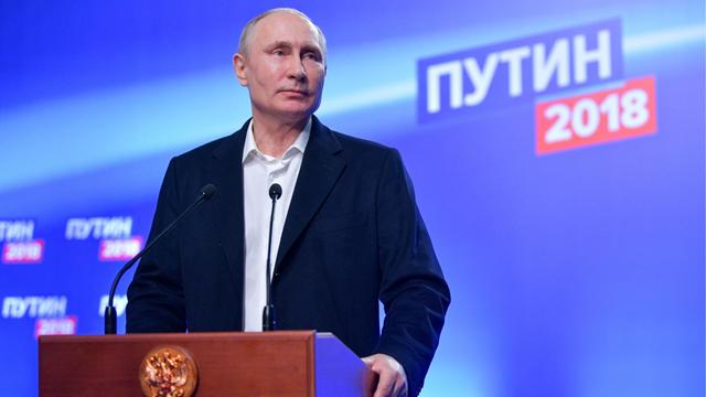Putin steht an einem Rednerpult und schaut in das (auf dem Foto nicht zu sehende) Publikum.