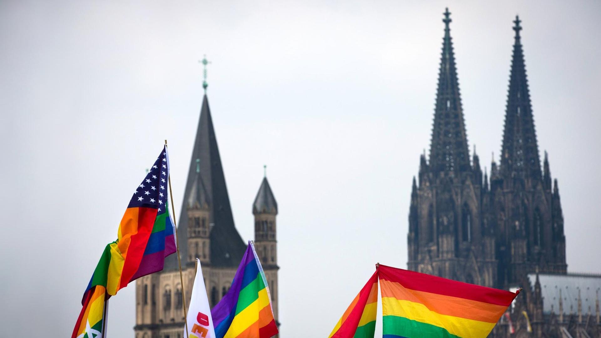 Regenbogen Fahnen im Vordergrund. Dahnter ist verschwommen der Kölner Dom zu sehen. Regenbogen Fahnen im Vordergrund. Dahnter ist verschwommen der Kölner Dom zu sehen.