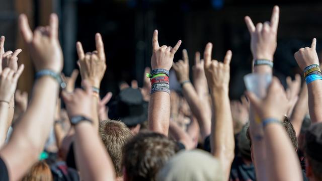 Metal-Fans feiern am 05.08.2016 in Wacken (Schleswig-Holstein) auf dem Festivalgelände des Wacken Open Air mit dem Metal-Gruß, der sogenannten Pommesgabel.
