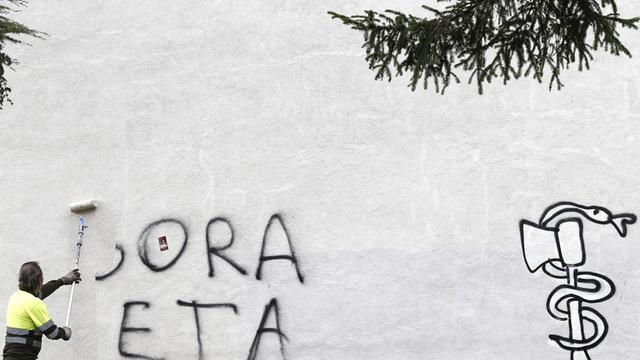 Mann entfernt ein Graffiti an einer weißen Wand, Text: "Gora ETA", übersetzt "Lang lebe ETA"