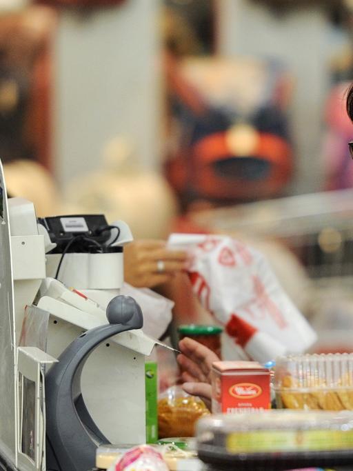Eine Frau steht zum Bezahlen in einem Supermarkt an der Kasse.