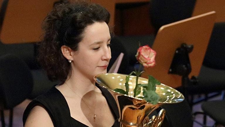 Hornistin hält ihr Horn mit Rose im Schallbecher Hornistin hält ihr Horn mit Rose im Schallbecher