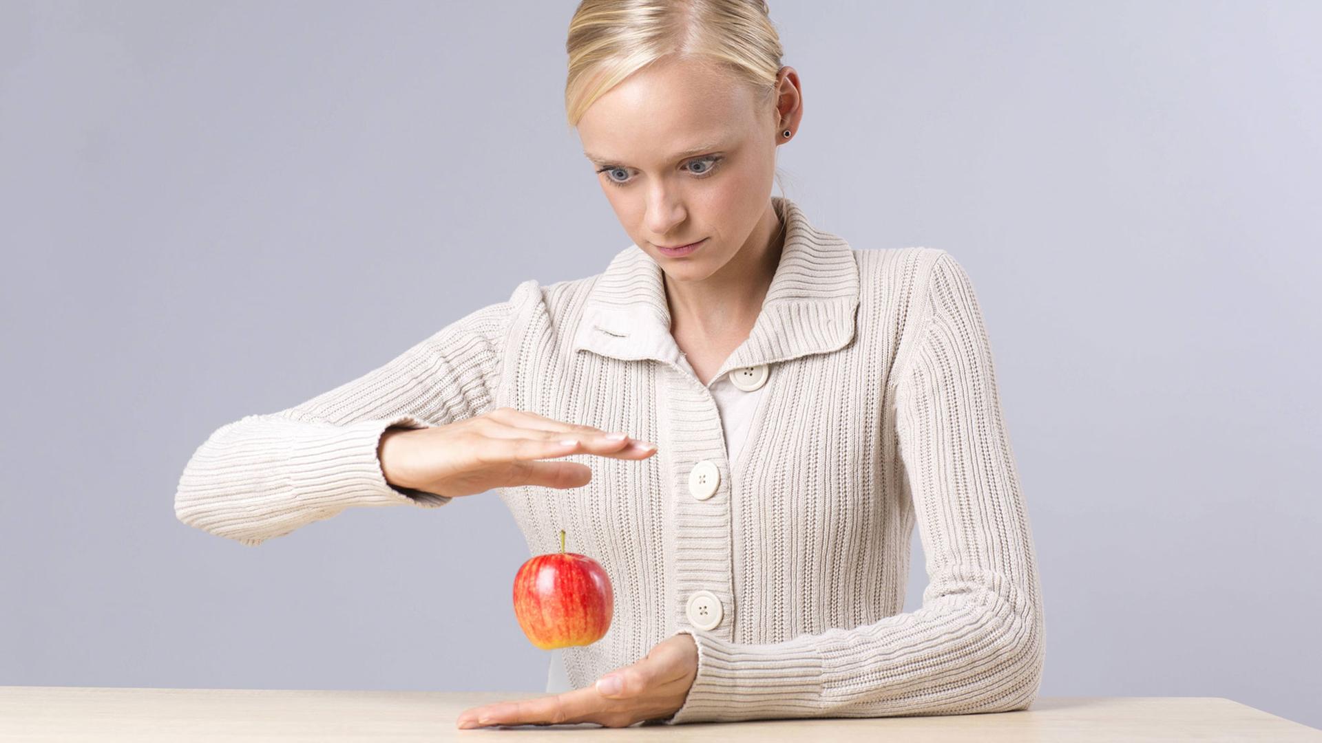 Eine junge Frau lässt einen Apfel zwischen ihen Händen schweben (Symbolfoto)