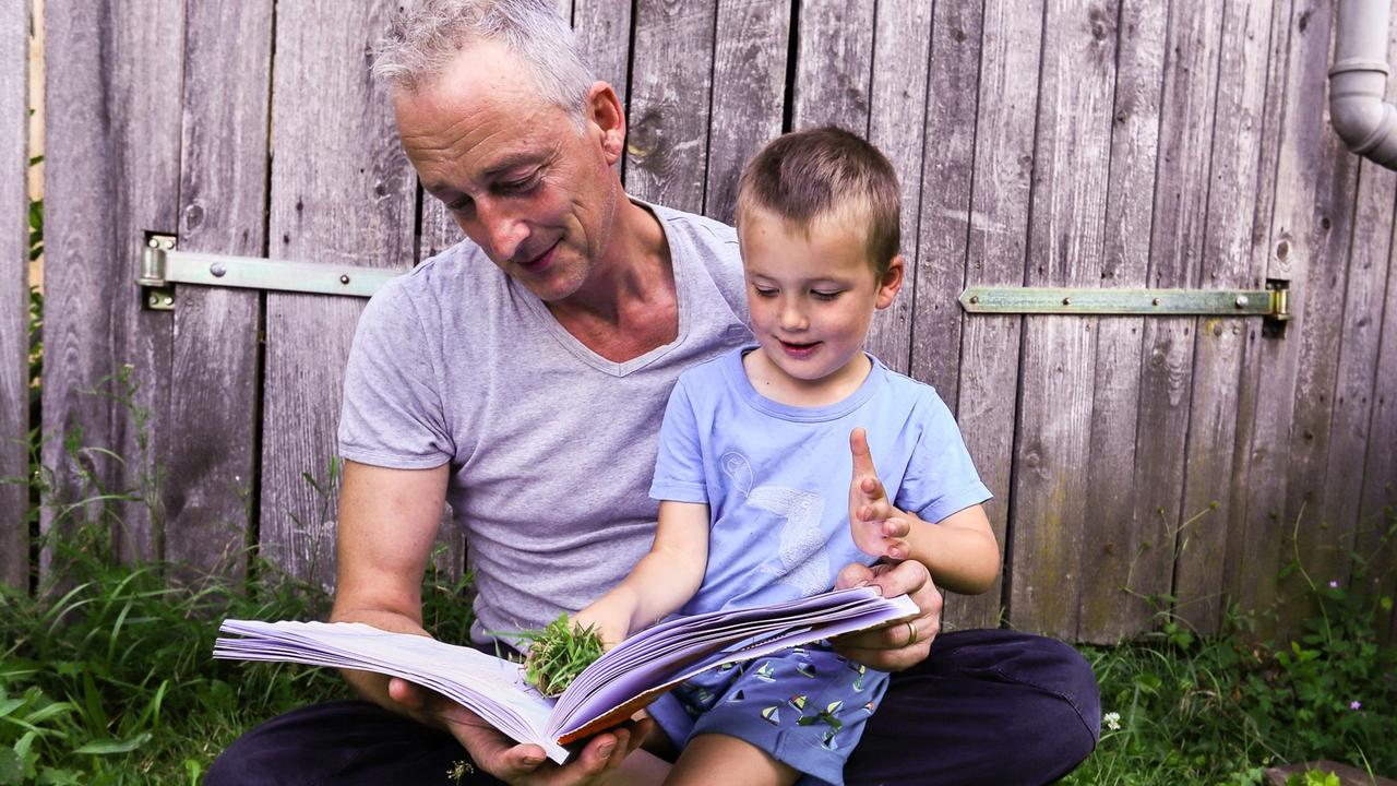 Der Autor und Journalist Heiner Kiesel mit einem Kind und einem aufgeschlagenen Buch auf dem Schoß