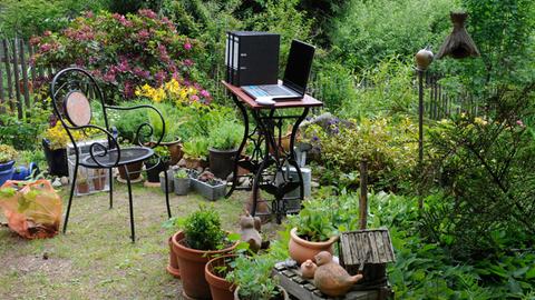 Arbeiten im Freien: Drei Aktenordner und ein Laptop auf einem Tisch in einem Garten.